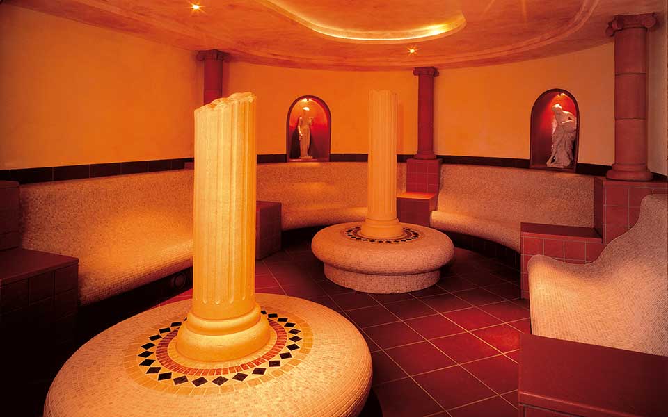 Interior of a Caldarium with a prominent pillar and two chairs, reflecting the ambiance of ancient Roman bathing culture.