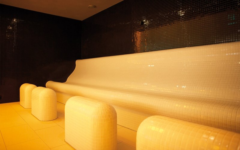 A white bench in a laconium room with tiled walls, designed for dry sweating at a comfortable temperature of 60°C.